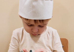 Chłopiec w czapce kucharskiej trzyma w ręku piernik.