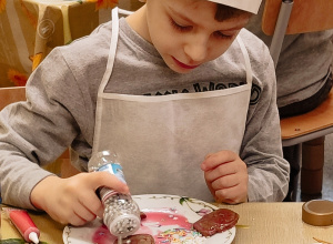 Chłopiec w czapce kucharskiej ozddabia pierniczki.