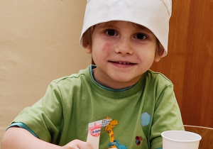 Chłopiec w czapce kucharskiej ozdabia pierniczki.