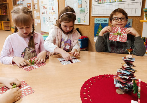 Dzieci siedzą przy stoliku. Wykonują kartki do św Mikołaja z kolorowych papierów.