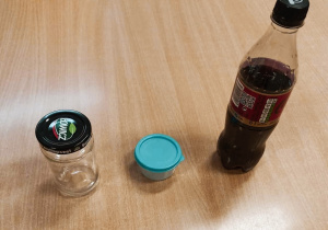 Na stoliku ustawione są słoik, kubeczek z próbką, butelka z cieczą.