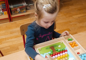 Dziewczynka układająca obrazek z kuleczek przy pomocy drewnianej pensety.