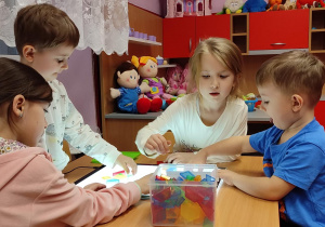 Dzieci siedzące przy stoliku, układają transparentne klocki na świetlnym ekranie.