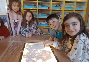 Dzieci rysujące w mące wysypanej na świetlnym monitorze.