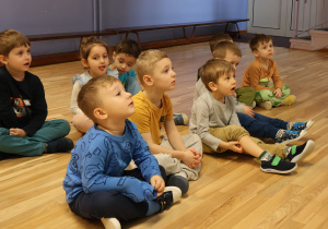 Dzieci siedzące w sali na podłodze.