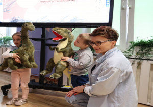 Prowadząca zajęcia nauczycielka z dziećmi trzymającymi maskotki przedstawiające dinozaury.