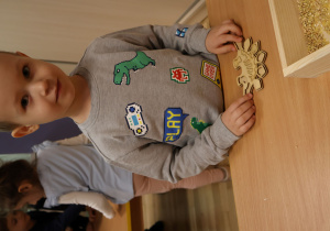 Chłopiec układający puzzle przedstawiające dinozaura.